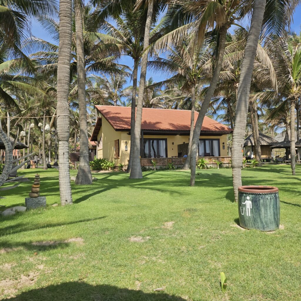 Single-story bungalow villa surrounded by palm trees and green lawns at Pandanus Resort in Mui Ne, Vietnam.