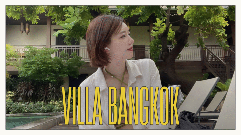 Woman sitting by the pool at Villa Prasumen Bangkok, surrounded by lush greenery and boutique hotel architecture. Text overlay: VILLA BANGKOK.