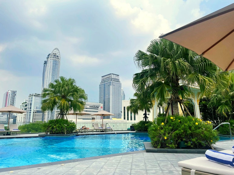 A sunny outdoor pool area at Chatrium Grand Bangkok with city skyscrapers in the background.